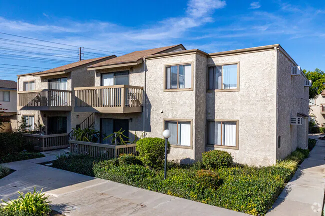 Two-story stucco apartment building with balconies and manicured hedges